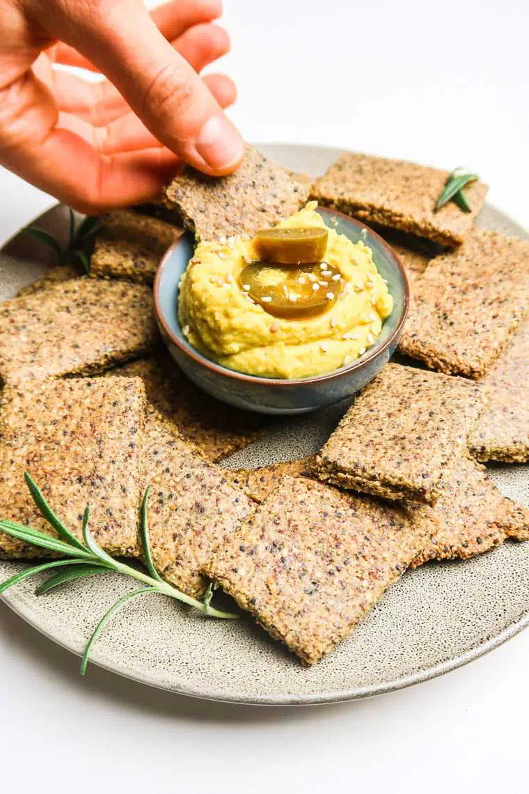 plate with over a dozen homemade quinoa tahini crackers and yellow dip