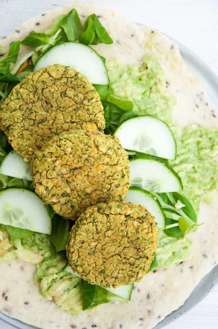 tortilla wrap on a white plate with avocado, lettuce, cucumber and spinach falafel