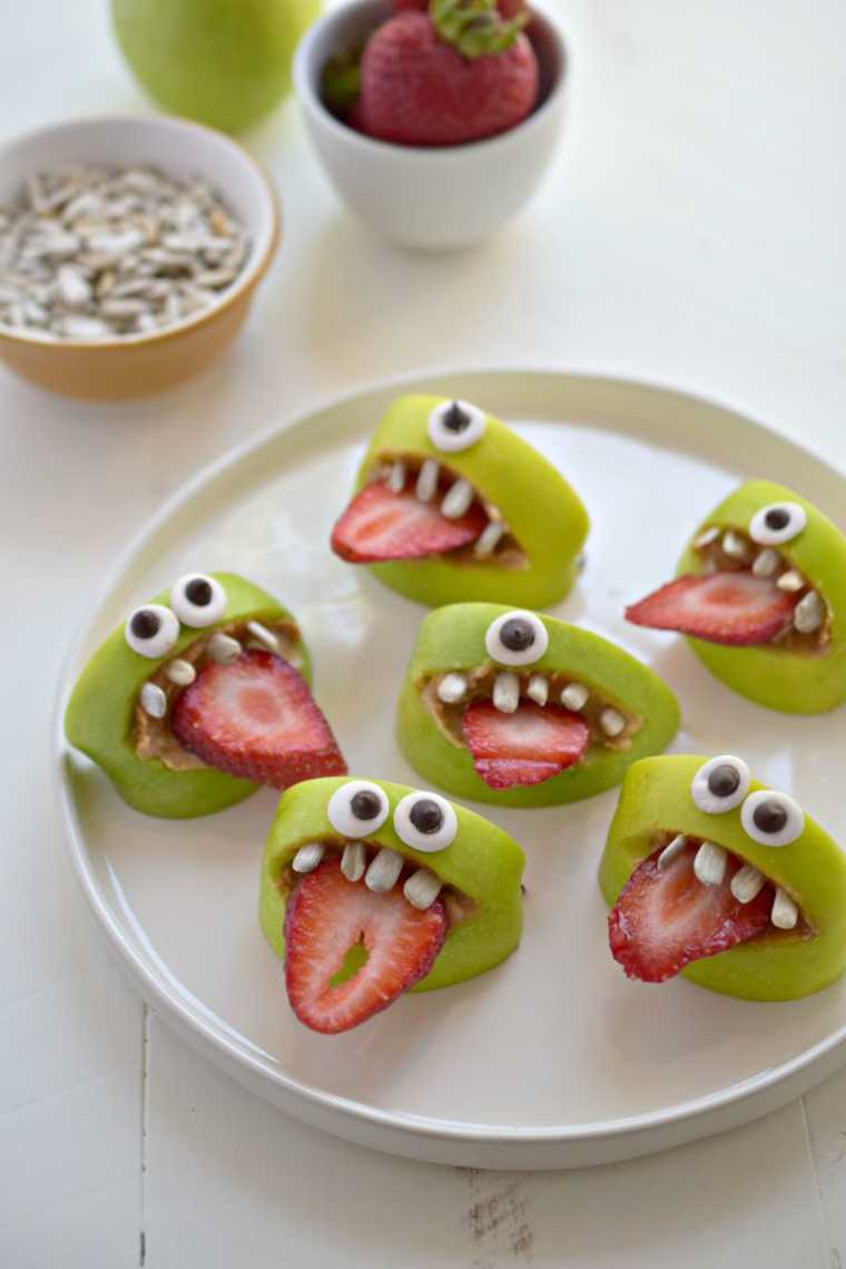 white plate with 6 apple slices with eyes, strawberry tongue and little teeth