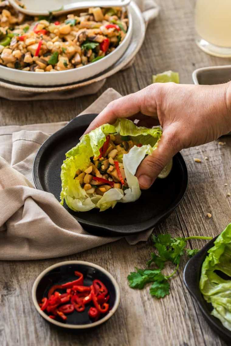 hand holding a vegan lettuce wrap called Mushroom San Choy Bow over a table