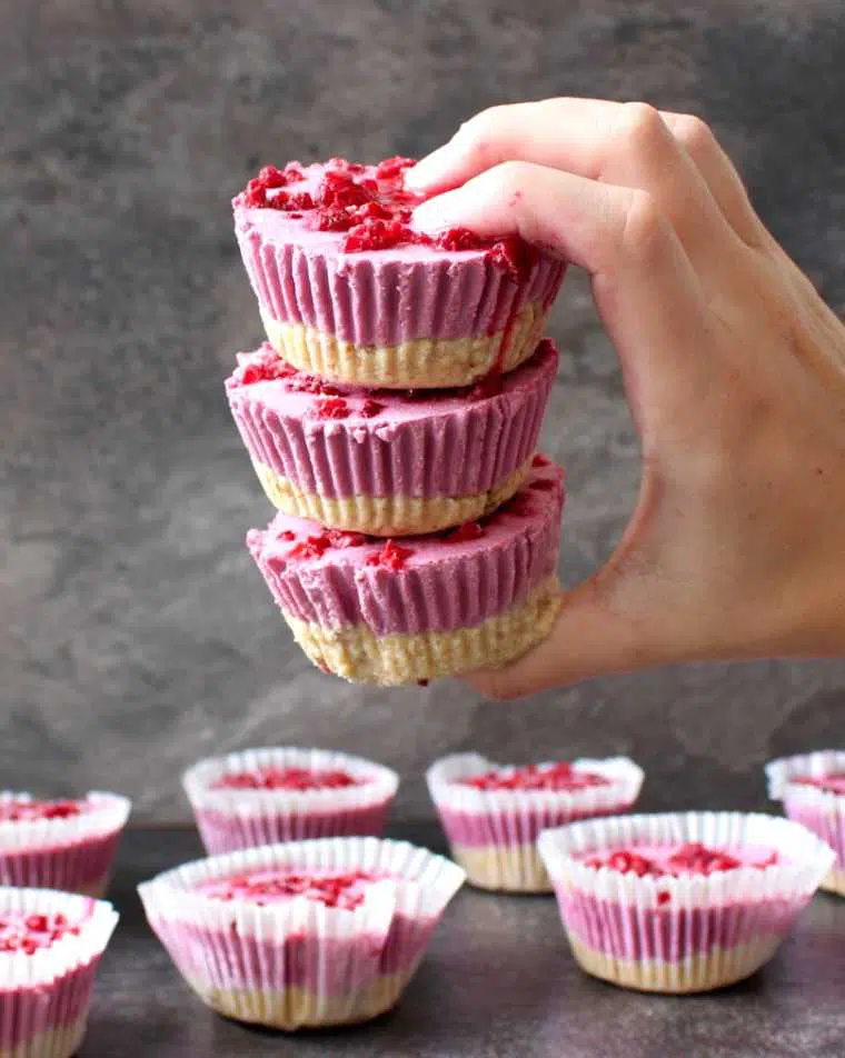hand holding three homemade raw vegan raspberry cheesecake cups over a table with more summer desserts