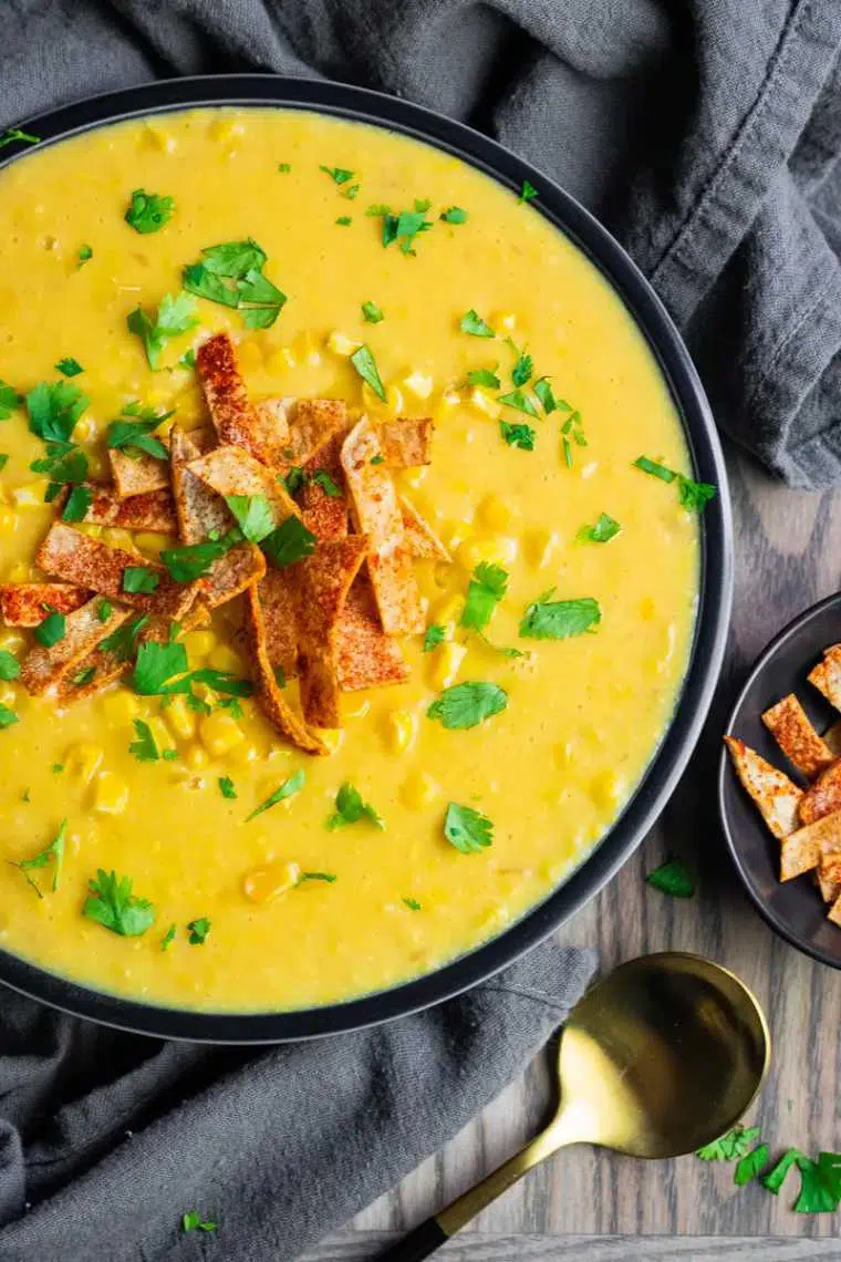 wooden table with a dark towel and a bowl of bright yellow vegan corn chowder