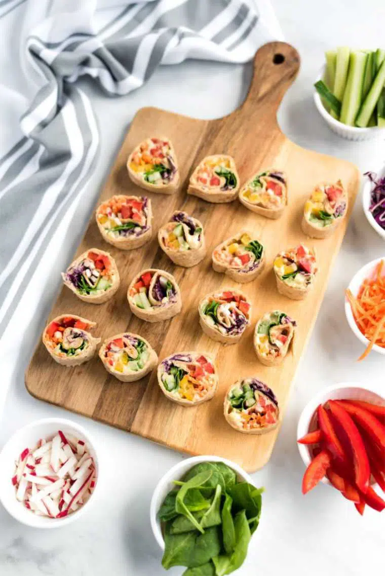 wooden chopping board with 16 small and colorful vegan vegetable pinwheels for a cold lunch