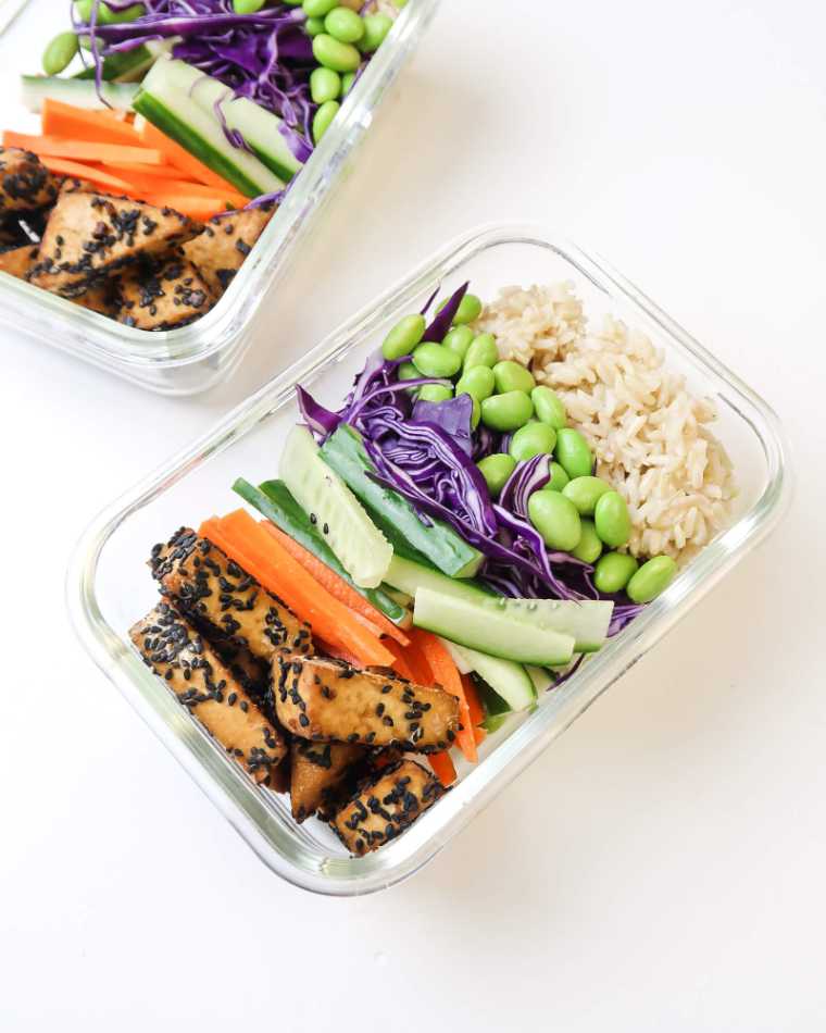 two glass containers filled with brown rice, edamame, carrot, cucumber, cabbage and baked tofu