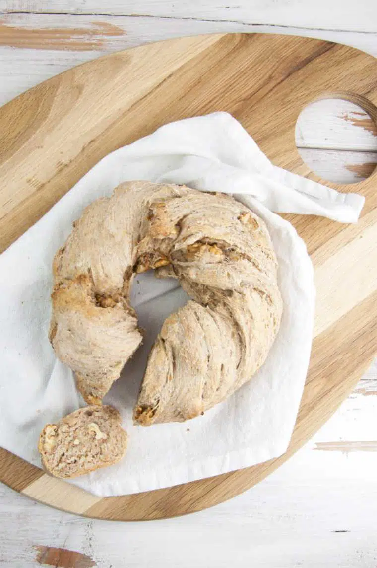 wooden surface with a white towel on which lays some homemade vegan walnut bread wreath