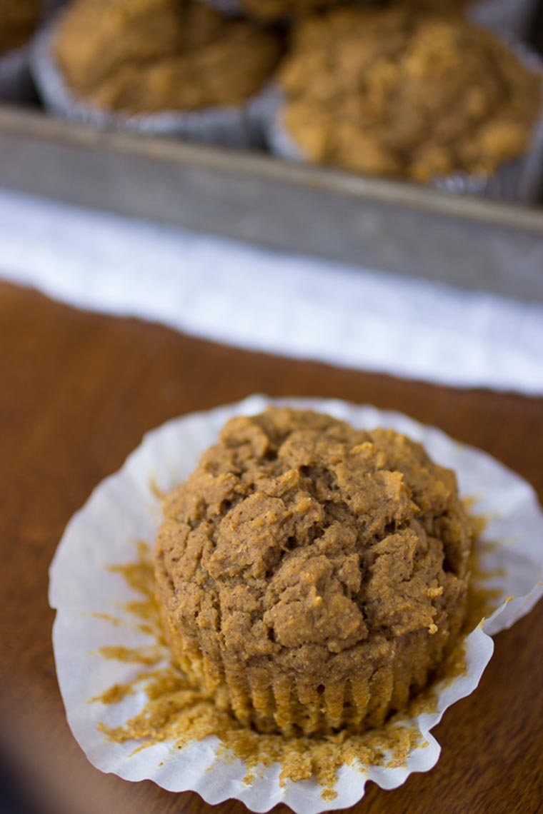 close up of a vegan pumpkin muffin in white paper cup on wooden surface