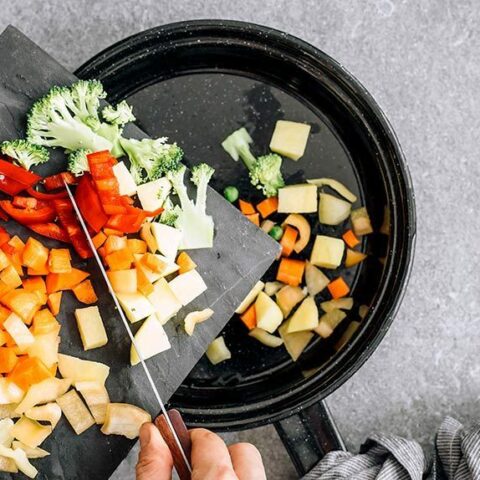 woman sauteing carrot, bell pepper and broccoli in a black pan with water instead of oil
