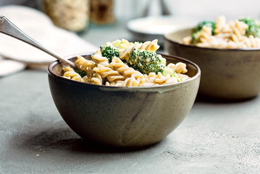 two bowls of vegan mac and cheese with broccoli standing on the counter