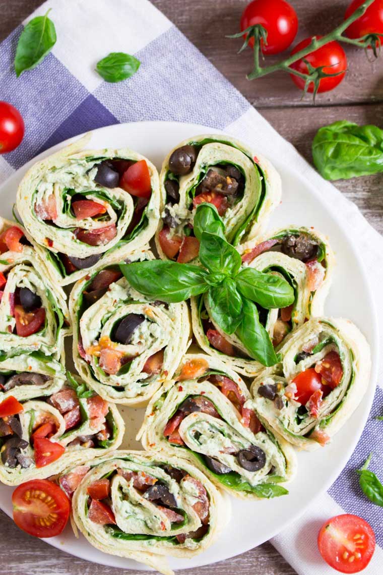 white plate with colorful basil tomato olive vegan ricotta pinwheels