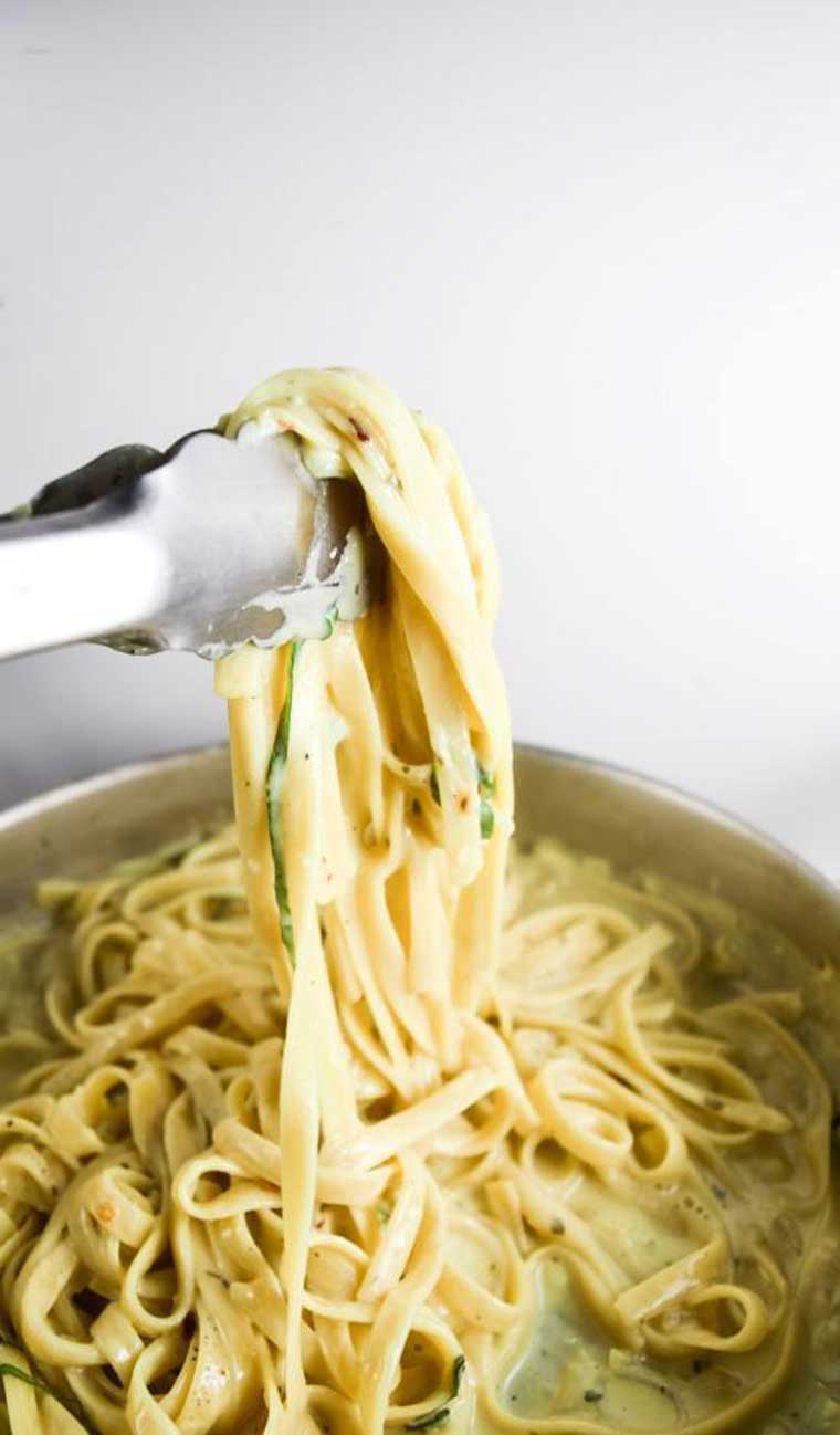 close up of a pot of creamy vegan alfredo garlic pasta being pulled up by tongs