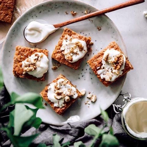 top view of 4 pieces of vegan carrot cake with cashew frosting on a grey plate next to a wooden spoon and black linen