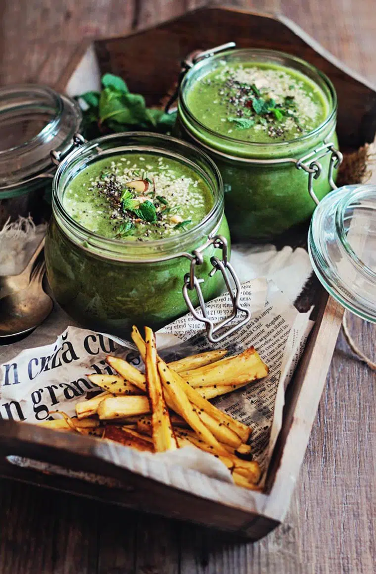 wooden tray with newspaper and sliced baked parsnip fries as well as two glass jars with green soup