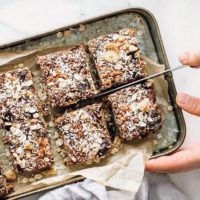 woman cutting baked vegan oat bars topped with coconut shreds into eight pieces