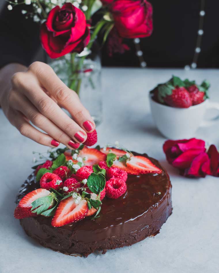 white table with some red roses and strawberries next to a vegan instant pot chocolate cake