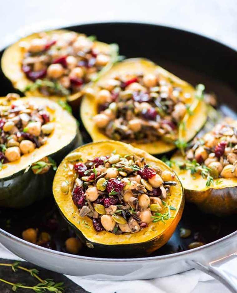 five acorn squash halved stuffed with seeds, chickpeas and dried fruit in a baking dish