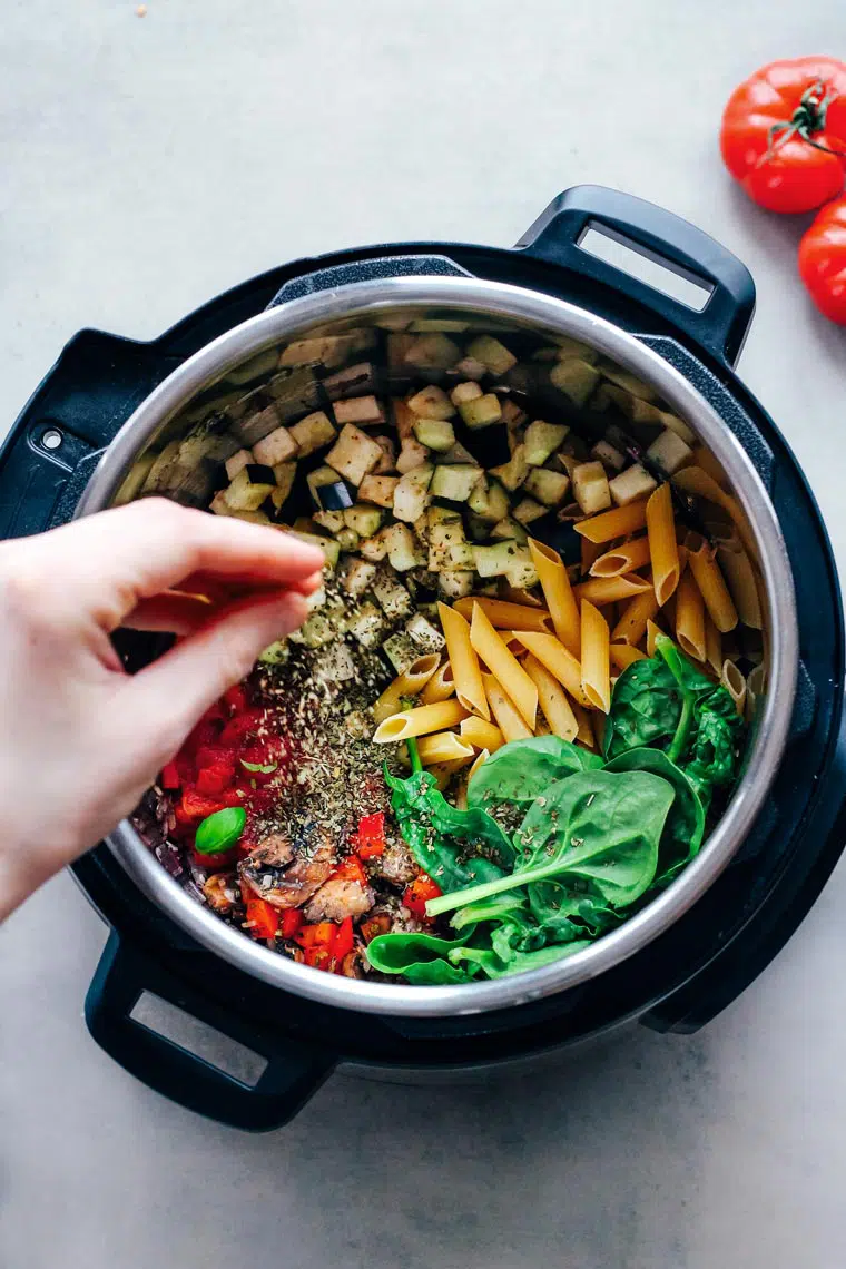 hand sprinkling dry spices into an Instant Pot filled with veggies and pasta