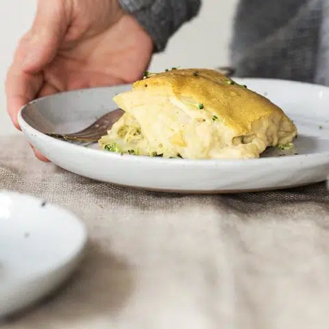 piece of vegan broccoli potato casserole on a white plate standing on some linen