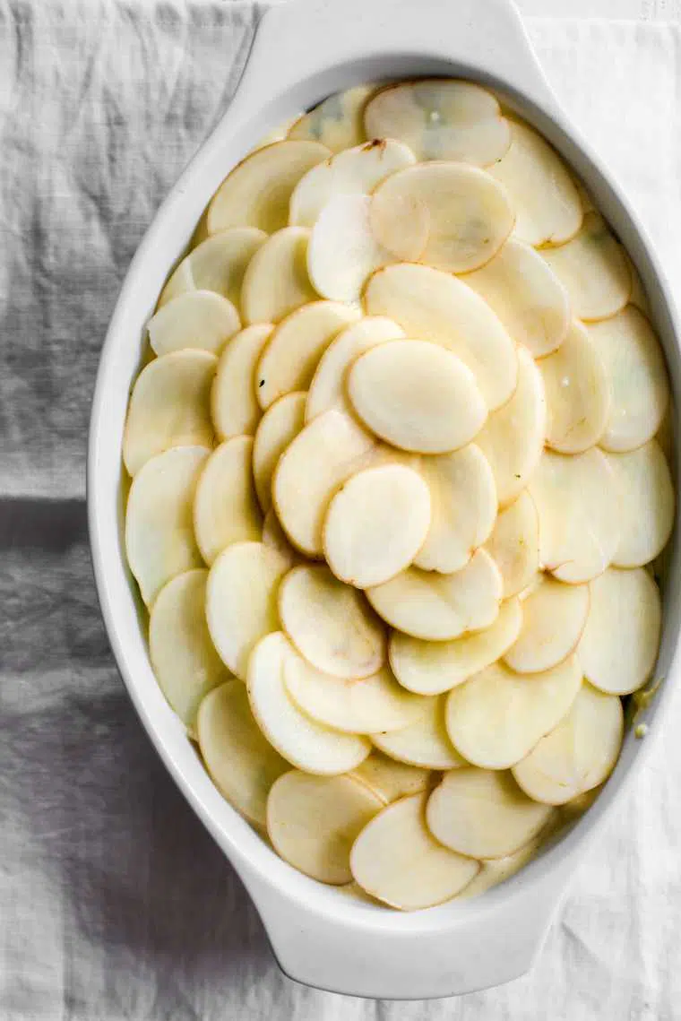white baking dish on a table with sliced potatoes