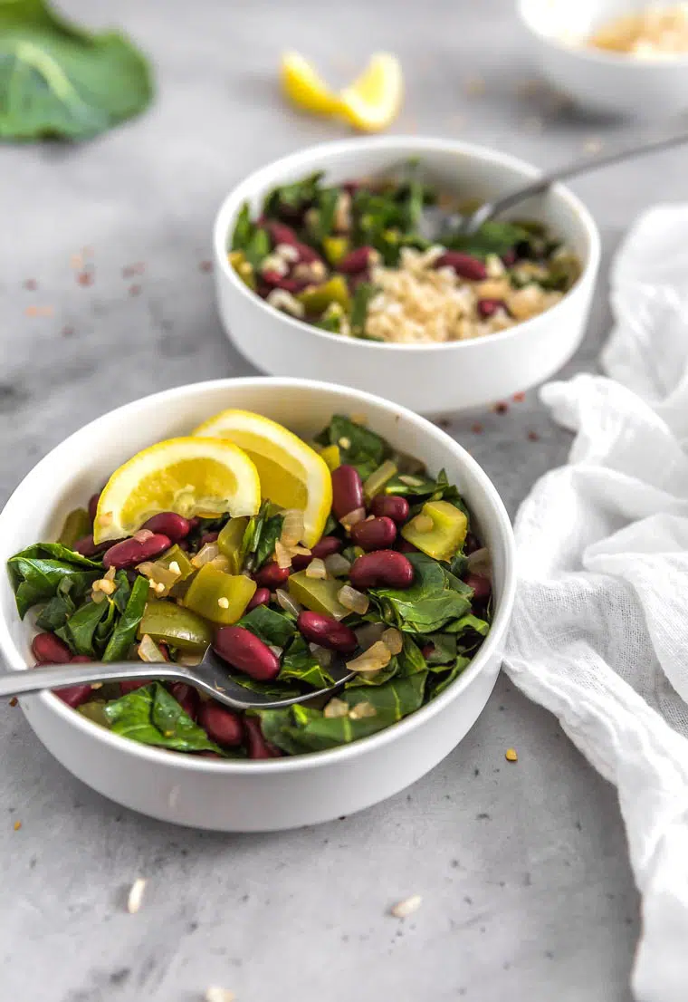two white bowls with oil-free vegan sauteed Southern collard greens, kidney beans and lemons