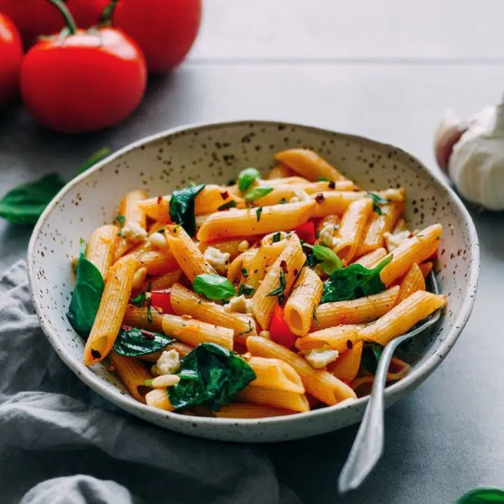 white speckled bowl with cooked penne and veggies in marinara sauce