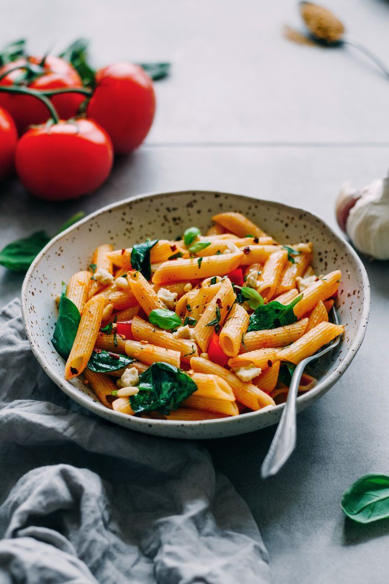 white speckled bowl with cooked penne and veggies in marinara sauce