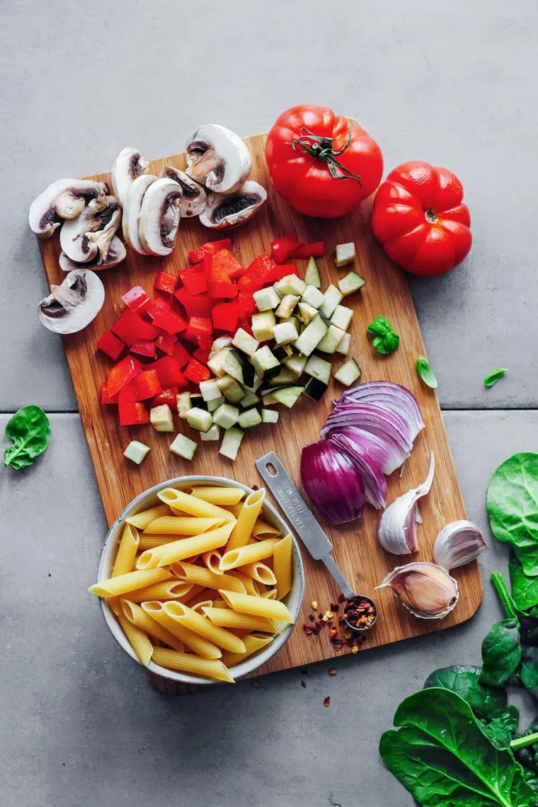 wooden chopping board with chopped vegetables, onions, tomatoes and dry pasta