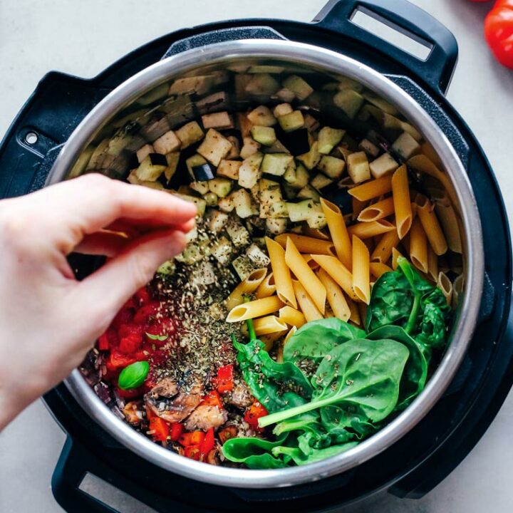 hand sprinkling dry spices into an Instant Pot filled with veggies and pasta