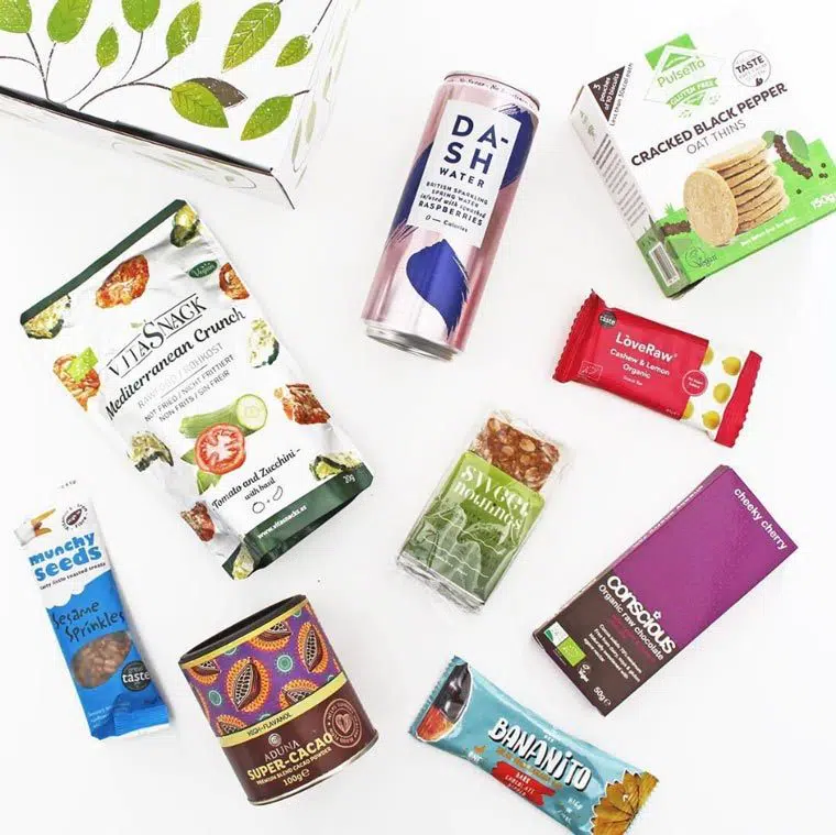 Overhead view of the contents of a snack box from The Goodness Project: Dash water, oat thins cacao powder and vegan bars
