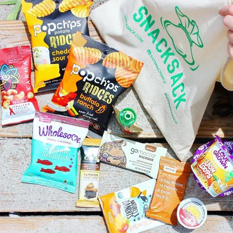 Different vegan snacks like protein bars, candies and chips on a wooden surface