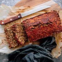 hearty vegan lentil loaf with red glaze on some parchment paper on a wooden chopping board
