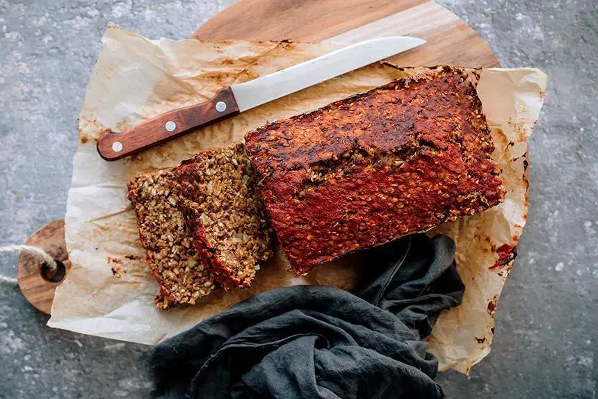 hearty vegan lentil loaf with red glaze on some parchment paper on a wooden chopping board