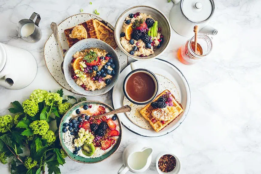 marble table with some flowers and lots of bright bowls filled with colorful vegan waffles and oatmeal with fruit