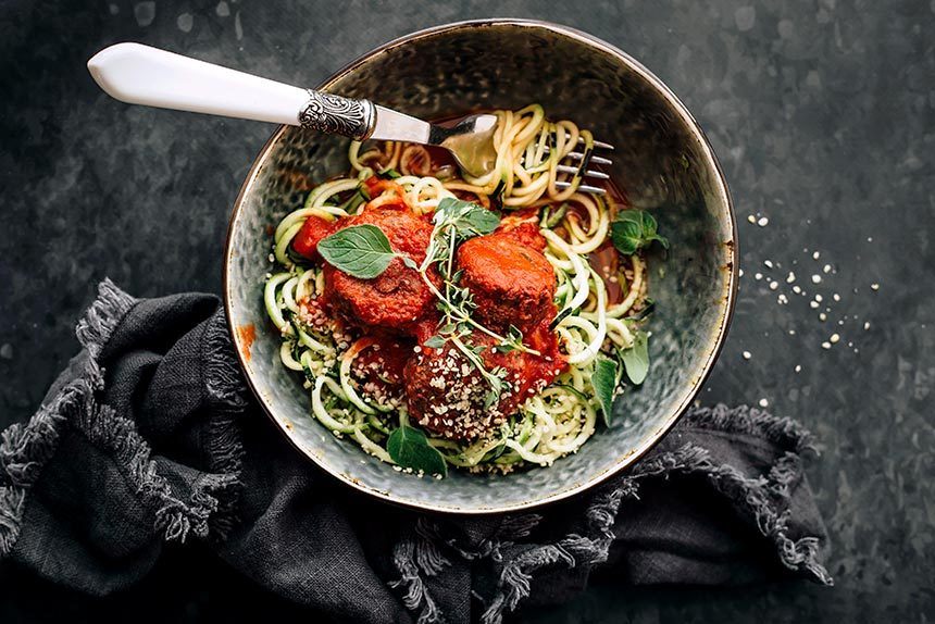 vegan black bean balls in marinara sauce with zucchini noodles and a fork in a dark bowl