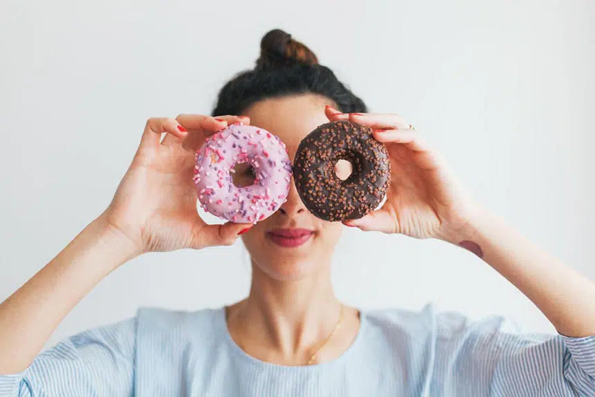 woman with bun craving junk food and holding a brown and a pink doughnut in front of her face