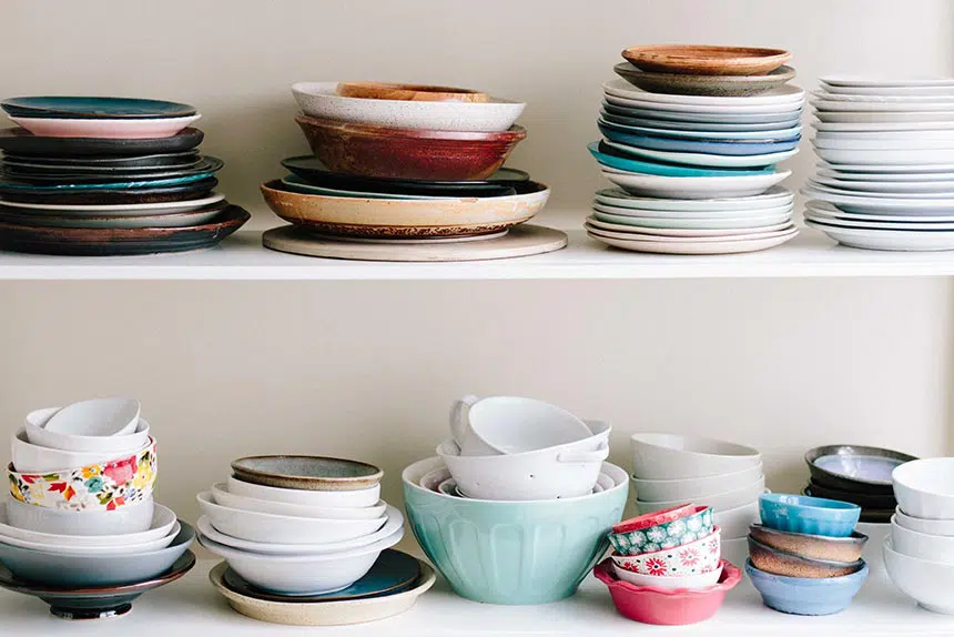 different colorful plates and bowls as part of more kitchen tools standing on a shelf