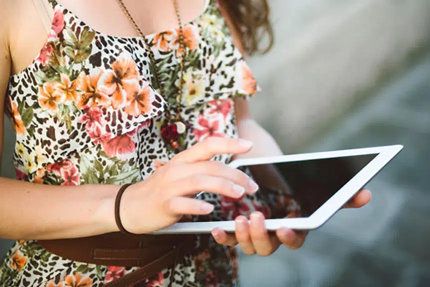 woman in floral dress standing with an ipad in her hand and scrolling with her finger