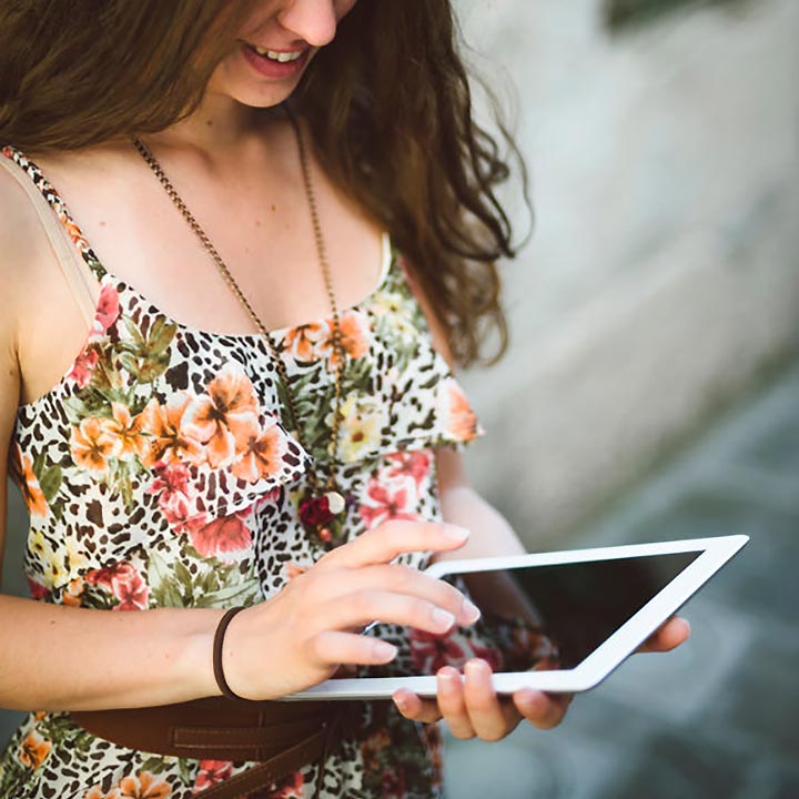 woman in floral dress standing with an ipad in her hand and scrolling with her finger