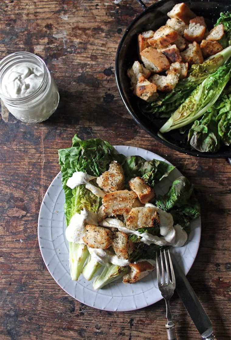 wooden table with a bowl and a plate of Vegan Caesar Salad