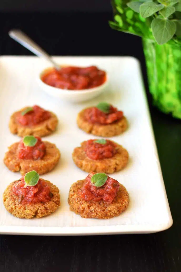 white plate with six cheesy quinoa bites topped with tomato sauce