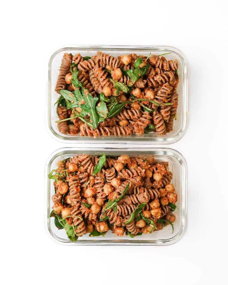 two glass containers with sundried tomato pesto pasta salad, greens and chickpeas for a portable vegan lunch