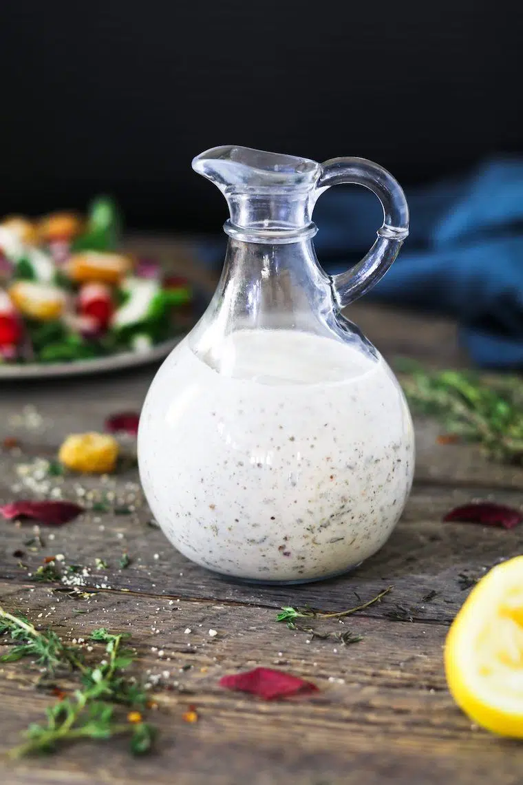 wooden table with fresh herbs and a glass jar containing creamy white vegan Italian dressing