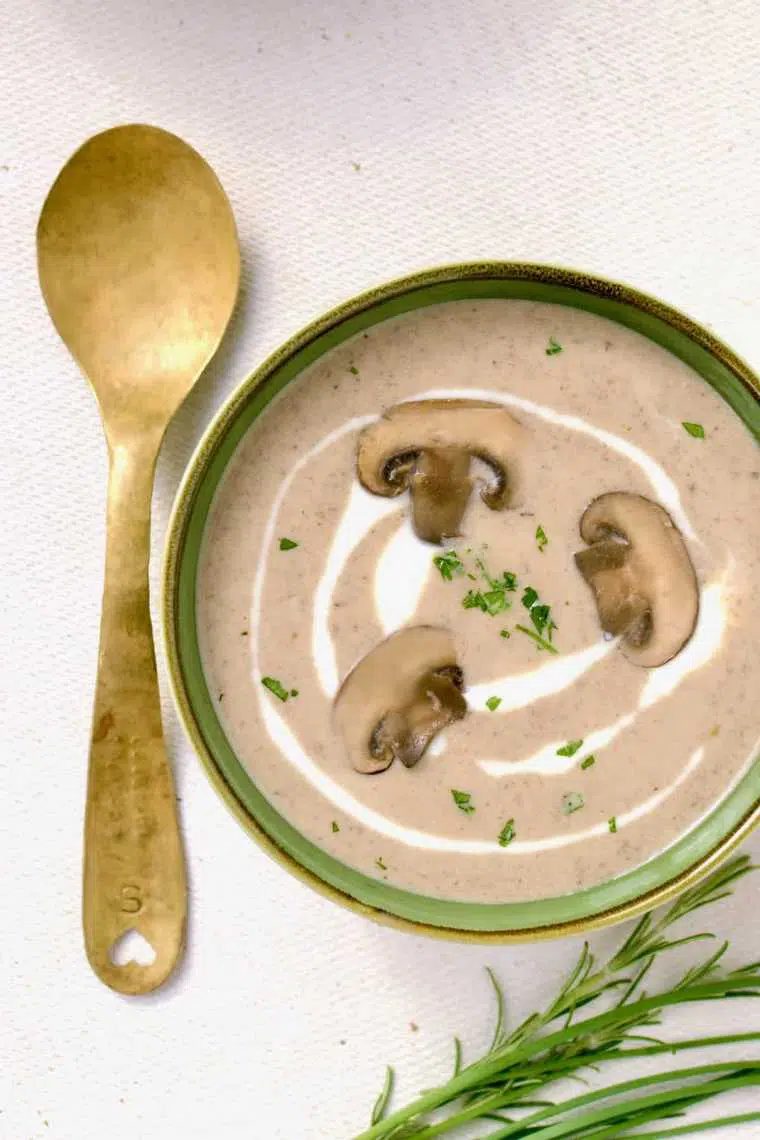 close up of a bowl of vegan mushroom soup with sliced mushroom and fresh herbs