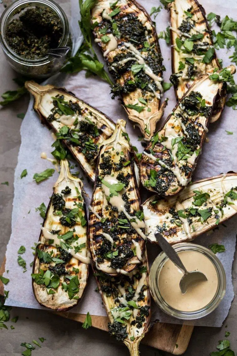 chopping board with parchment paper on which eight slices of grilled aubergine that have been filled with lentils and drizzled with tahini lie