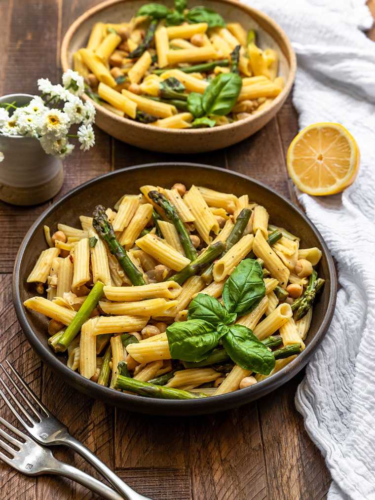 two bowls on a table with cooked penne and asparagus in a lemon garlic sauce