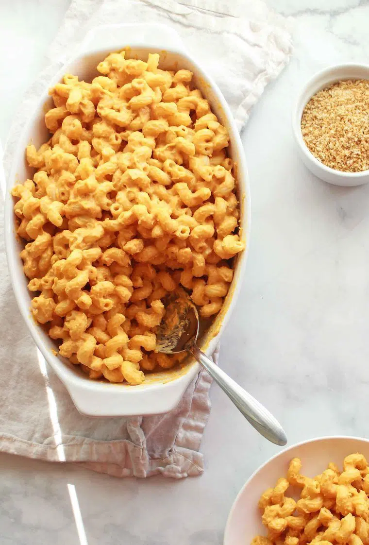 white baking dish with creamy vegan sweet potato mac and cheese and a spoon
