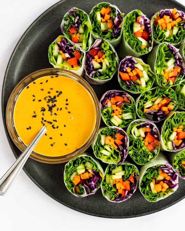 dark plate with 19 little colorful veggie rolls and orange dip