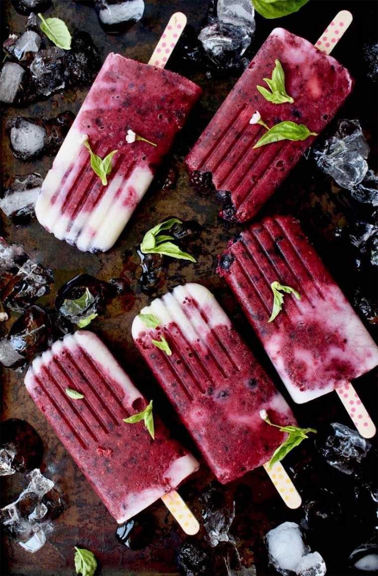 dark table with five dark red vegan fruit popsicles next to some ice cubes