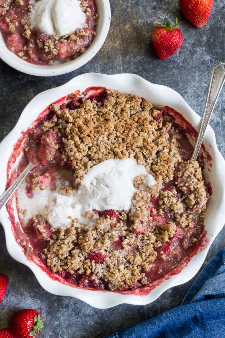 white baking dish with vegan strawberry crumble, two spoons and some melted ice cream