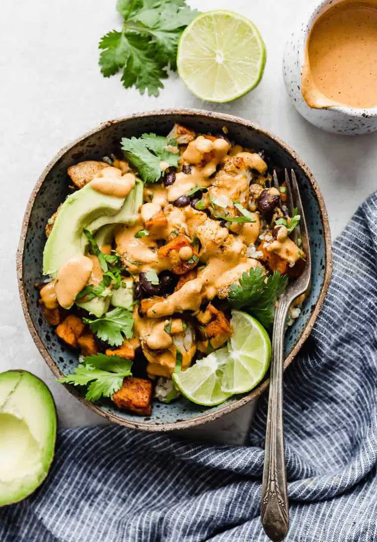 speckled bowl with roasted cauliflower, beans, lime, avocado and a creamy sauce