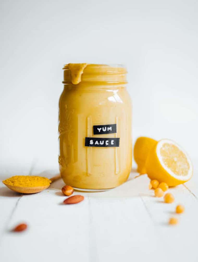 white table with some chickpea, almonds, lemon and a glass jar labeled "yum sauce" filled with yellow thick sauce